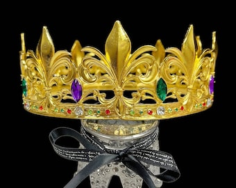 以下が含まれることがあります： 花柄のデザインとカラフルな宝石がついた金の王冠。王冠は「Happy Jewelry World」という文字が書かれた白黒の台の上に置かれています。