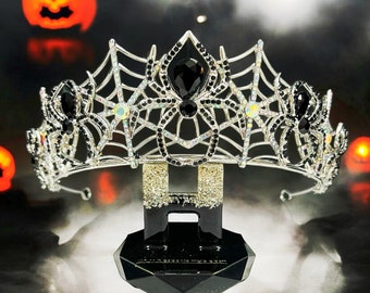 May include: A silver spiderweb crown with black crystal accents. The crown is sitting on a black pedestal.