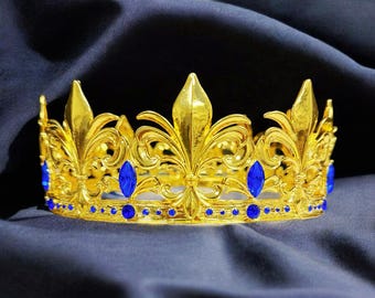 以下が含まれることがあります： 青い宝石が付いた金の王冠。王冠は百合の花の模様で、小さな丸い宝石で飾られています。
