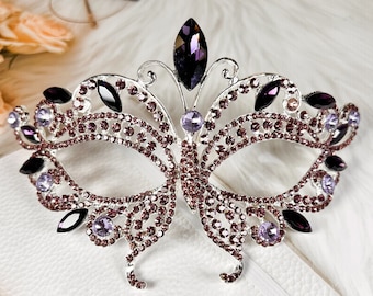 May include: A silver butterfly-shaped masquerade mask with purple and clear rhinestones. The mask has a delicate design and is perfect for a costume party or a special occasion.