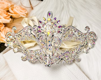 May include: A silver masquerade mask with an intricate design and iridescent rhinestones. The mask has a delicate, feminine look and is perfect for a costume party or a special occasion.