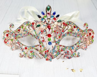 Peut inclure: Un masque de bal de couleur or avec un design délicat et complexe. Le masque est orné de strass et de cristaux colorés, créant un look éblouissant et festif.