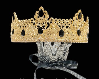 May include: A gold-colored crown with black gemstones, displayed on a decorative glass stand. The crown features an ornate design with intricate details. A black ribbon with white text is tied around the stand. The text "Happy Jewelry World" is at the bottom.