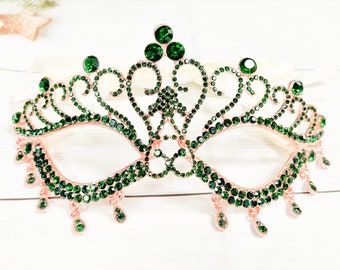 Può includere: Una maschera da ballo verde e oro rosa con un design a corona e cristalli pendenti.