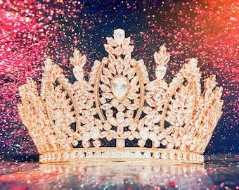 May include: A sparkling gold crown with a large, clear crystal in the centre. The crown is adorned with smaller crystals and has a pointed top.