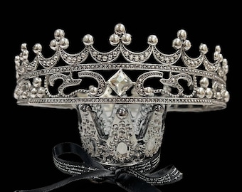 May include: A silver crown with a large clear rhinestone in the center. The crown is decorated with small silver beads and has a pointed top.