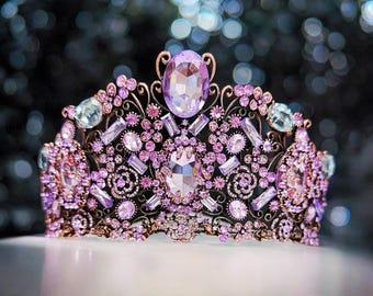May include: A delicate crown with a silver base and purple and pink rhinestones. The crown is adorned with intricate floral designs.