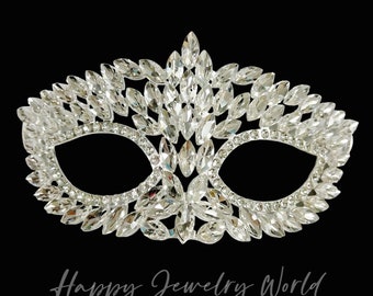 Op de afbeelding: Een zilveren masker voor een maskerade met een delicaat ontwerp van strass. Het masker heeft twee ooggaten en is versierd met een patroon van kleine, glinsterende kristallen.