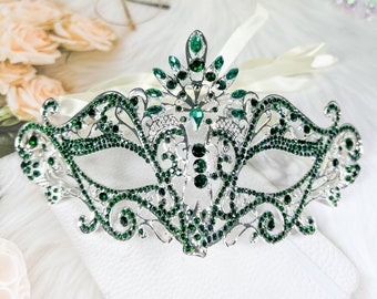 May include: A silver masquerade mask with a delicate design and green rhinestones. The mask is decorated with intricate details and is perfect for a masquerade ball or costume party.