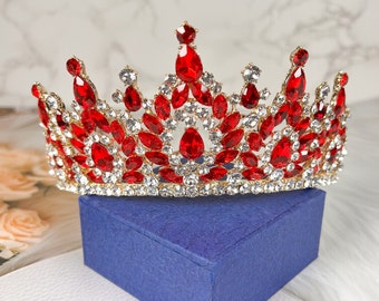 May include: A gold crown with red and clear rhinestones. The crown is on a blue velvet box.