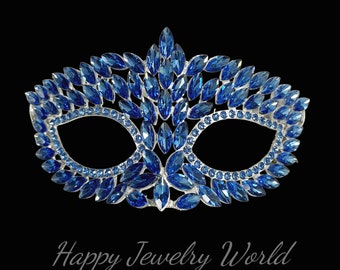 May include: A blue masquerade mask with a silver frame and rhinestones. The mask is decorated with a pattern of leaves and flowers.