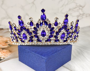 May include: A gold crown with blue and clear rhinestones. The crown is on a blue velvet box.