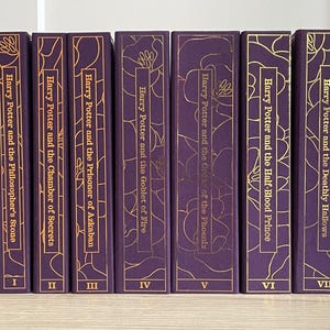 以下が含まれることがあります： 金色の文字とイラストが施された、紫色のハードカバーの書籍7冊セット。書籍のタイトルは、「ハリー・ポッターと賢者の石」、「ハリー・ポッターと秘密の部屋」、「ハリー・ポッターとアズカバンの囚人」、「ハリー・ポッターと炎のゴブレット」、「ハリー・ポッターと不死鳥の騎士団」、「ハリー・ポッターと謎のプリンス」、「ハリー・ポッターと死の秘宝」です。