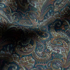 May include: Close-up of a dark teal fabric with a detailed paisley pattern. The design features swirling, teardrop-shaped motifs in shades of brown, orange, and pink, creating a rich, textured appearance. The fabric has a subtle sheen.