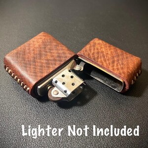 May include: A brown leather lighter case with white stitching. The case is open and the lighter is not included. "Lighter Not Included" is written in white text on a black background.