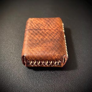 May include: A brown leather lighter case with a stitched border. The case has a distressed look and is made of high-quality leather.