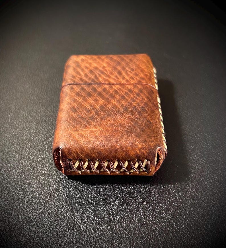 May include: A brown leather lighter case with a stitched border. The case has a distressed look and is made of high-quality leather.