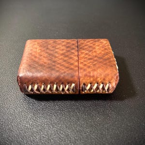 May include: A brown leather cigarette case with white stitching around the edges.