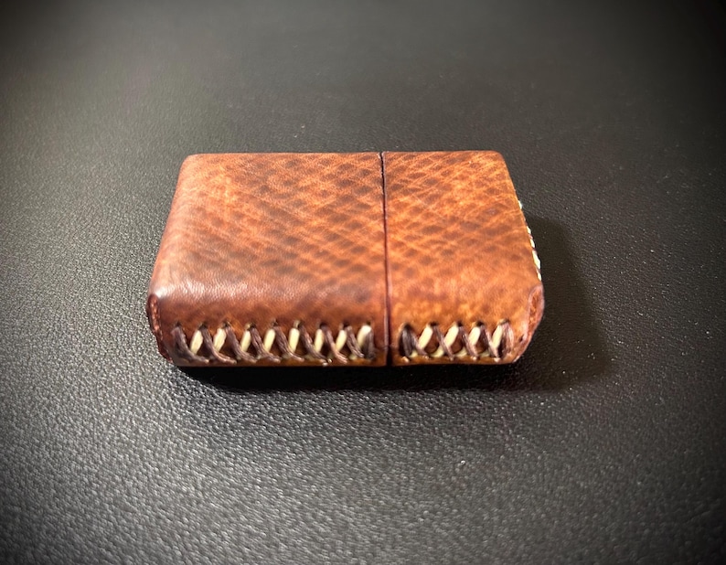 May include: A brown leather cigarette case with white stitching around the edges.