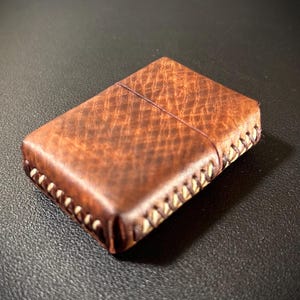 May include: A brown leather lighter case with white stitching around the edges.
