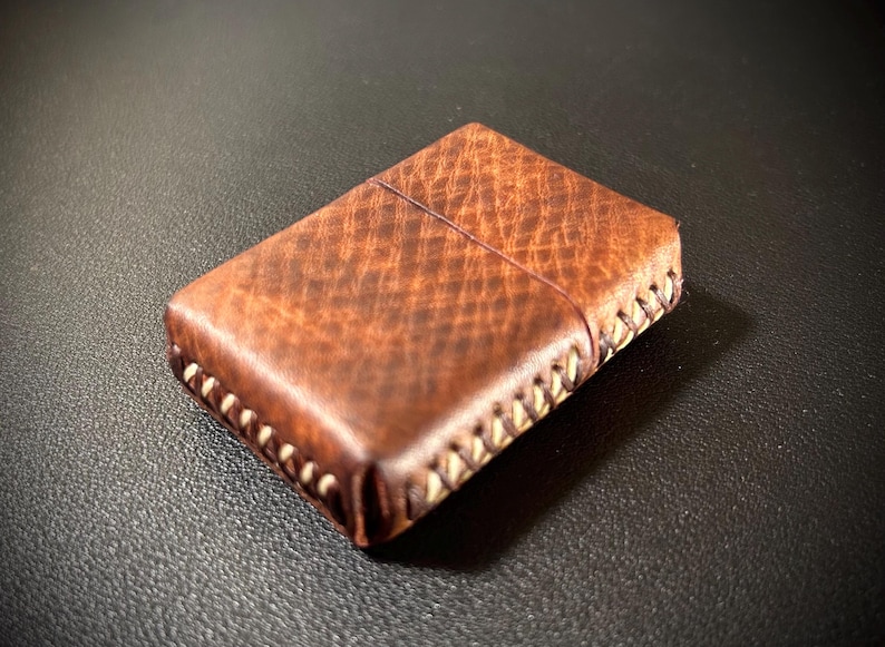May include: A brown leather lighter case with white stitching around the edges.