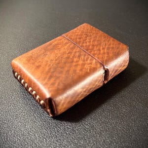 May include: A brown leather lighter case with white stitching around the edges.