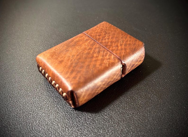 May include: A brown leather lighter case with white stitching around the edges.