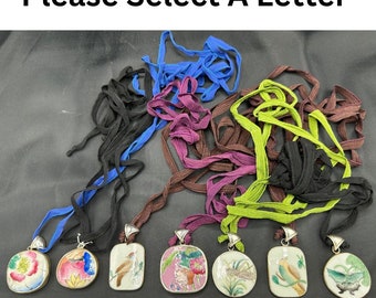 May include: Seven pendants with different designs, each on a colorful ribbon. The pendants are round and feature a variety of floral and bird motifs. The ribbons are blue, brown, purple, green, and black. The pendants are labeled A through G.