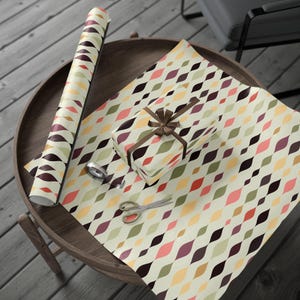 Puede incluir: Un rollo de papel de regalo con un patr&oacute;n geom&eacute;trico de formas onduladas de colores sobre un fondo crema. Una caja de regalo est&aacute; envuelta con el mismo papel y atada con una cinta marr&oacute;n. Tambi&eacute;n se ven tijeras y cinta adhesiva.