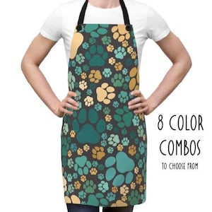 May include: An apron featuring a paw print design in teal, gold, and light blue on a dark grey backdrop. It has a black neck strap and the text "8 COLOR COMBOS TO CHOOSE FROM".