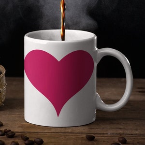 May include: A white coffee mug with a large pink heart design. Coffee is being poured into the mug.