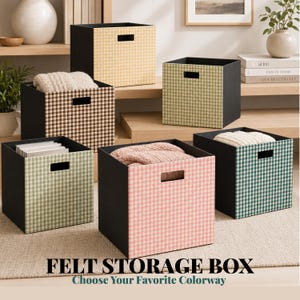 May include: A collection of six square felt storage boxes featuring a gingham pattern in various colors including yellow, brown, green, and pink. Each box has a black interior and a rectangular cutout handle on the front panel for easy carrying.