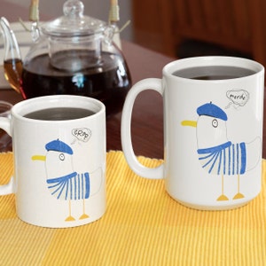 May include: Two white ceramic mugs with a cartoon seagull design. The mug on the left has the word "Crap" in a thought bubble above the seagull. The mug on the right has the word "Merde" in a thought bubble above the seagull.