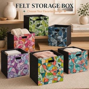 May include: Six square felt storage boxes with black sides and front panels featuring colorful, abstract stained-glass style patterns in green, pink, blue, purple, and multi-colored designs. Each box has a rectangular cutout handle on the front.