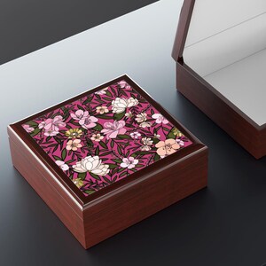 May include: A square wooden keepsake box with a dark brown finish and a hinged lid. The top of the lid features a vibrant magenta background decorated with a dense pattern of light pink and white flowers, green leaves, and dark stems.