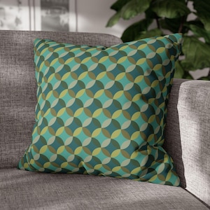 May include: Square throw pillow with a geometric pattern of overlapping circles in shades of teal, green, and yellow. The pillow is placed on a gray sofa, offering a decorative accent for home decor.