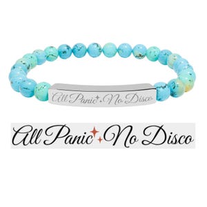 May include: A beaded bracelet featuring turquoise-colored beads and a silver bar. The bar is engraved with the phrase "All Panic No Disco" in a cursive font. The bracelet is displayed on a white background.