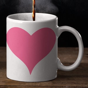 May include: A white coffee mug with a pink heart design. The mug is filled with coffee and steam is rising from the top.