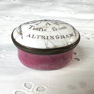 May include: A white porcelain trinket box with a pink base. The lid has a floral design and the text "A Trifle from ALTRINGHAM".