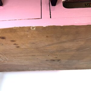 May include: A vintage pink cabinet with a wooden bottom and metal legs. The cabinet has two drawers with black handles. The word "STERILIZER" is visible on the top.