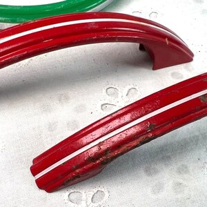 May include: Two red metal cabinet door handles with white trim. The handles are curved and have a simple design.