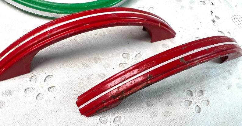 May include: Two red metal cabinet door handles with white trim. The handles are curved and have a simple design.