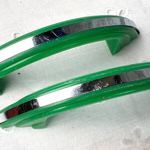 May include: Two vintage green cabinet door pulls with a silver metal accent. The pulls are curved and have a smooth, glossy finish.
