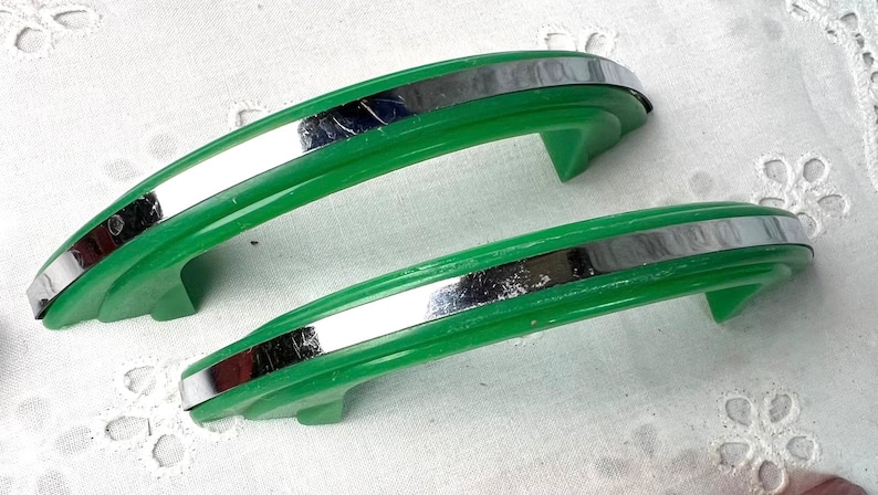 May include: Two vintage green cabinet door pulls with a silver metal accent. The pulls are curved and have a smooth, glossy finish.