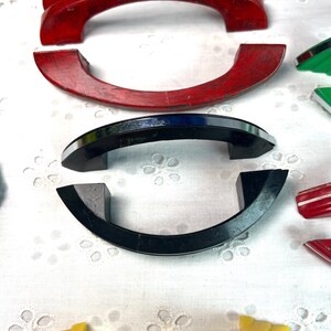 May include: Assortment of vintage cabinet door pulls in various colors and styles.  The pulls are made of wood, metal, and plastic.  The pulls are in various shapes, including arched, rounded, and rectangular.
