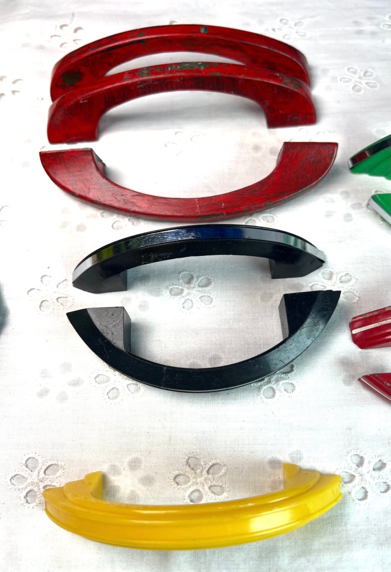 May include: Assortment of vintage cabinet door pulls in various colors and styles.  The pulls are made of wood, metal, and plastic.  The pulls are in various shapes, including arched, rounded, and rectangular.