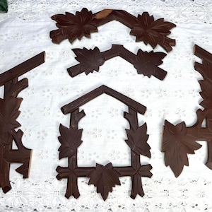 May include: Five wooden pieces of a cuckoo clock, each with intricate carvings of leaves and branches. The pieces are dark brown and have a rustic, antique look.