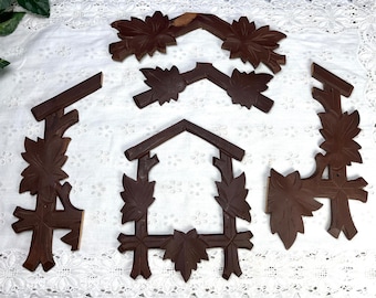 May include: Five wooden pieces of a cuckoo clock, each with intricate carvings of leaves and branches. The pieces are dark brown and have a rustic, antique look.