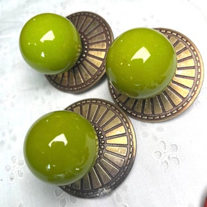 May include: Three green ceramic knobs with a brass-colored base. Each knob has a decorative design of concentric circles.