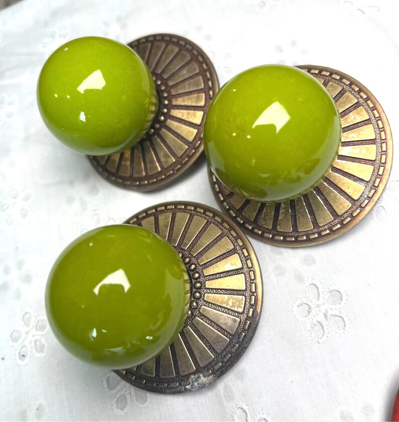 May include: Three green ceramic knobs with a brass-colored base. Each knob has a decorative design of concentric circles.